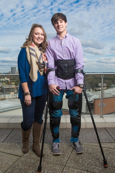 man wearing exoskeleton and using crutches stands next to able-bodied woman