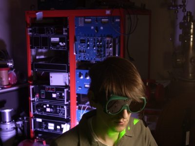 A man wearing safety goggles overseeing a green laser in a darkened lab