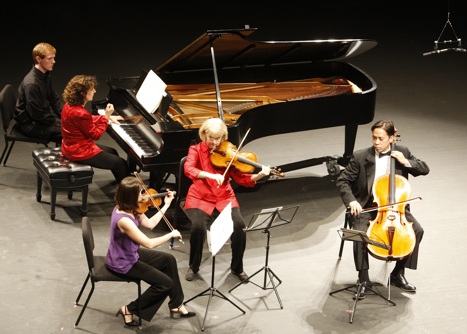 A piano quartet (piano, violin, viola, cello) plays on a concert stage.