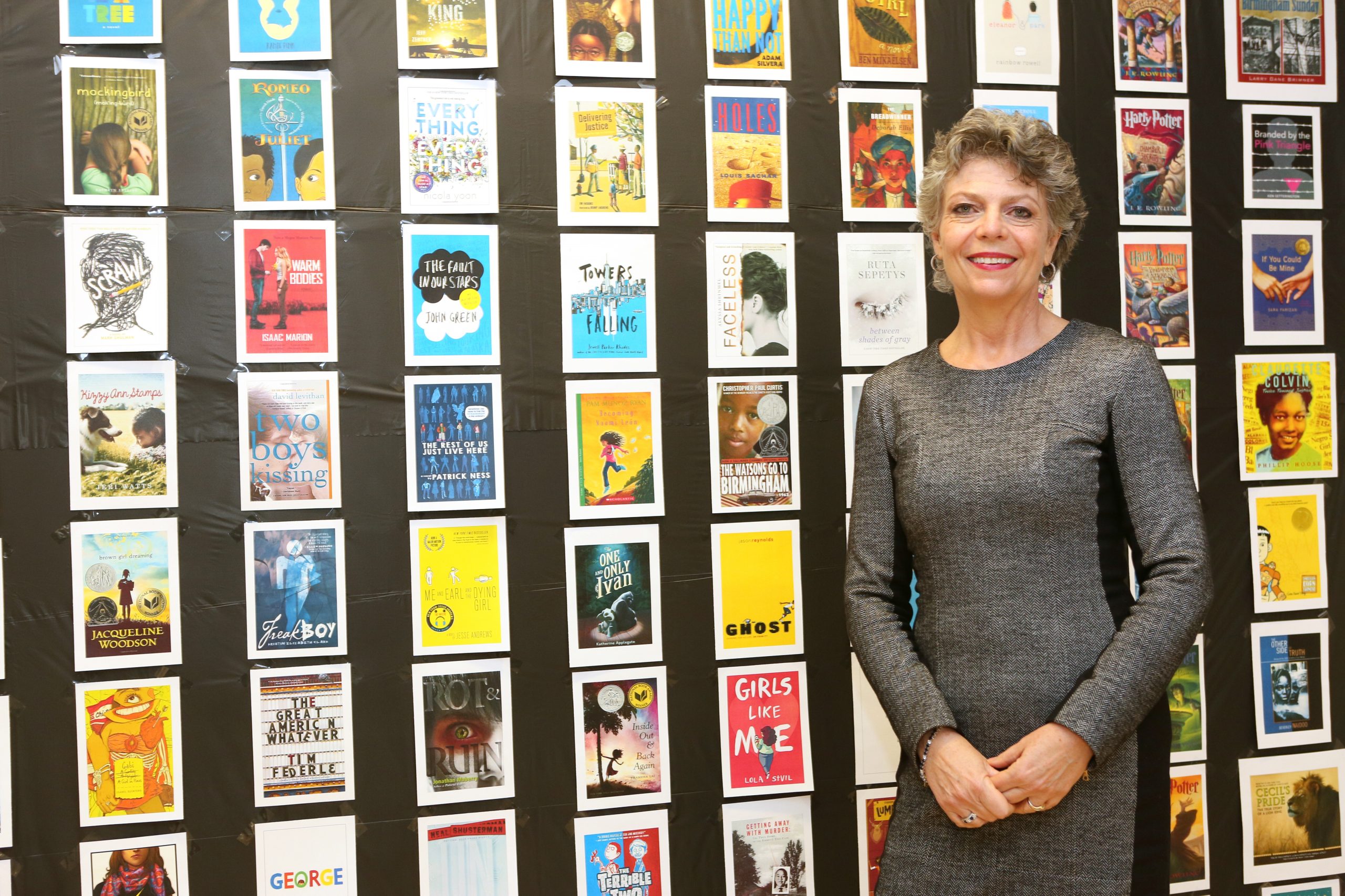 Camilla Benbow stands in front of a wall featuring book covers. 