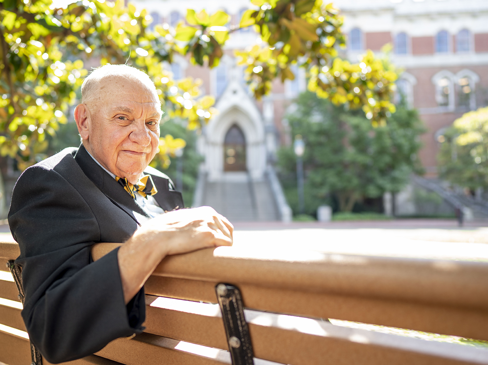 Dean Emeritus K.C. Potter sits on a bench on the Vanderbilt campus with the Kirkland Hall front steps in the background.