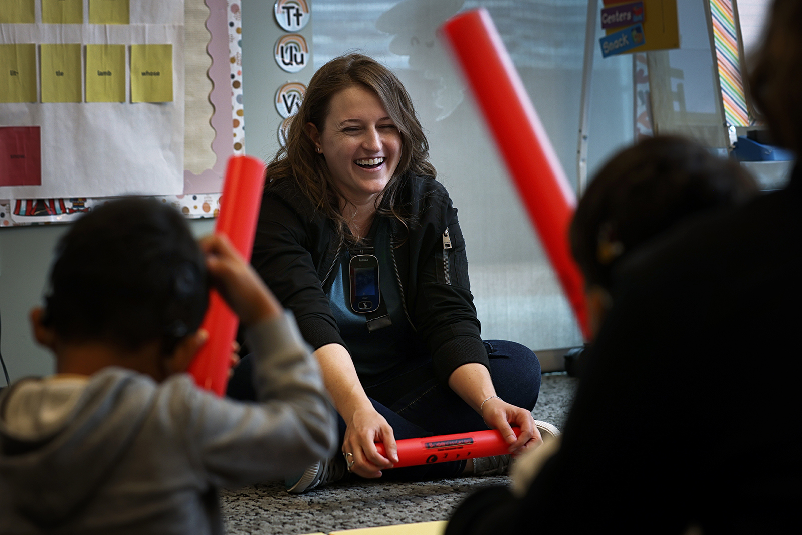 A young woman uses colorful plastic Boomwhackers to help preschoolers with hearing loss experience music. 