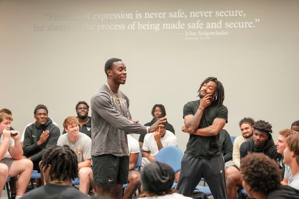 One student points during a discussion with another student standing pensively in the background.