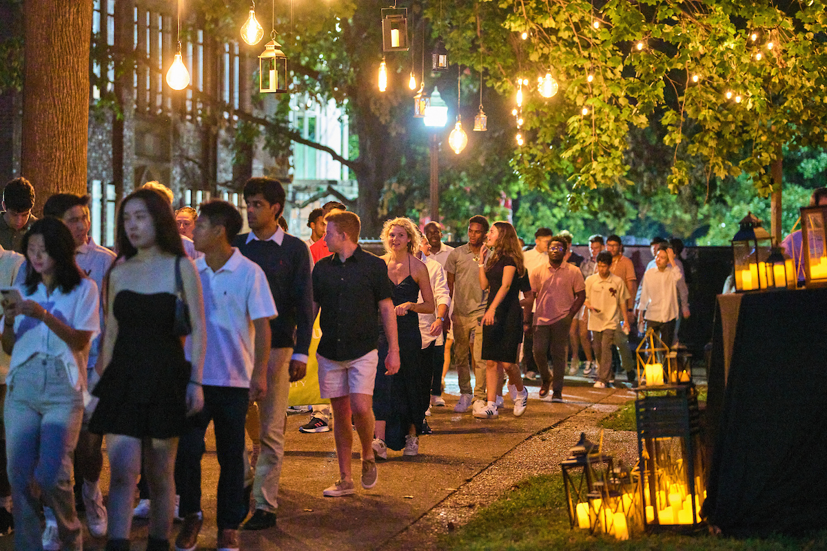 Students walking along a path lit by lanterns on the ground and hanging from trees