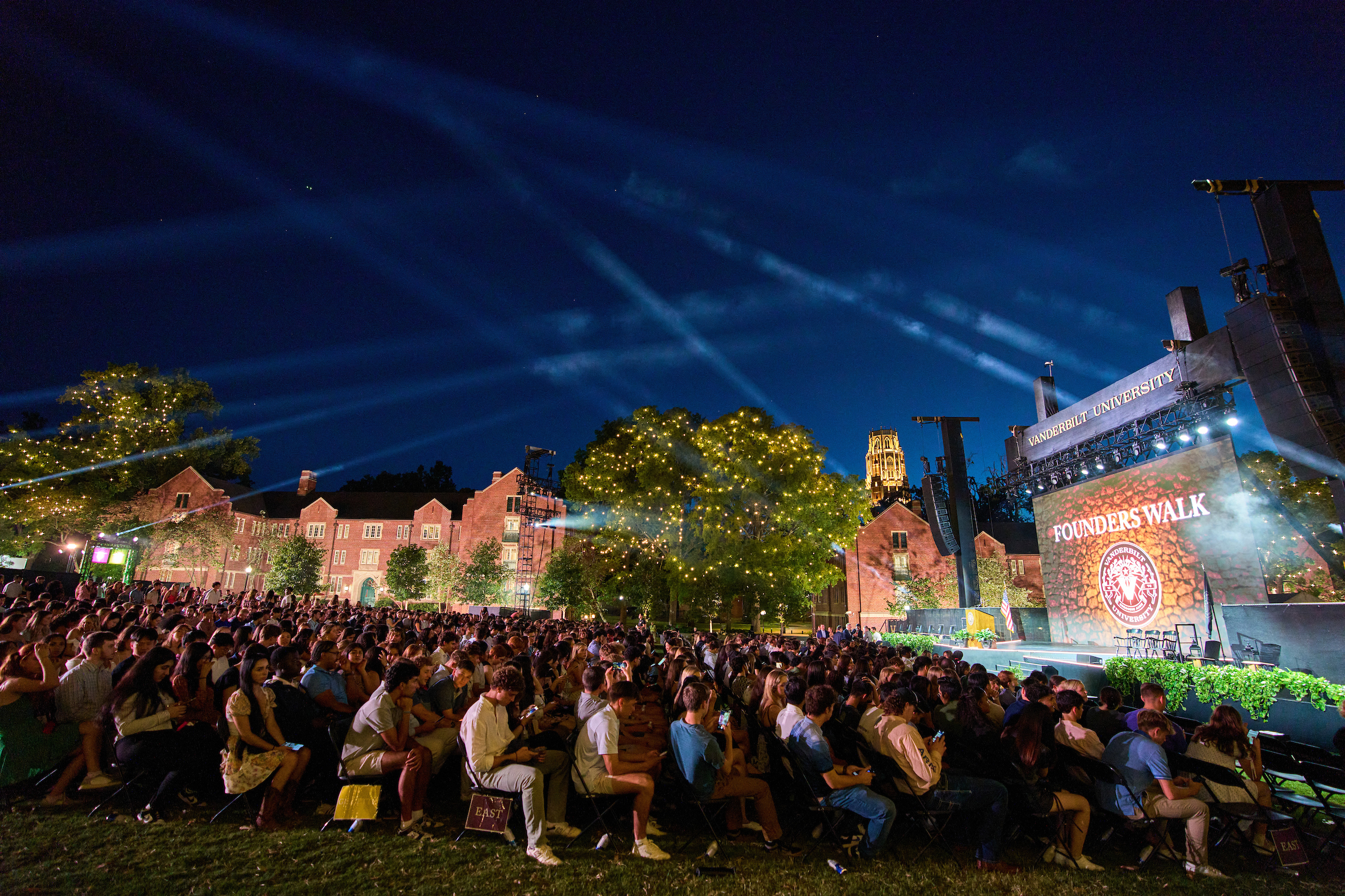 Alumni lawn at dusk with a stage and seated audience set up for Founders Walk