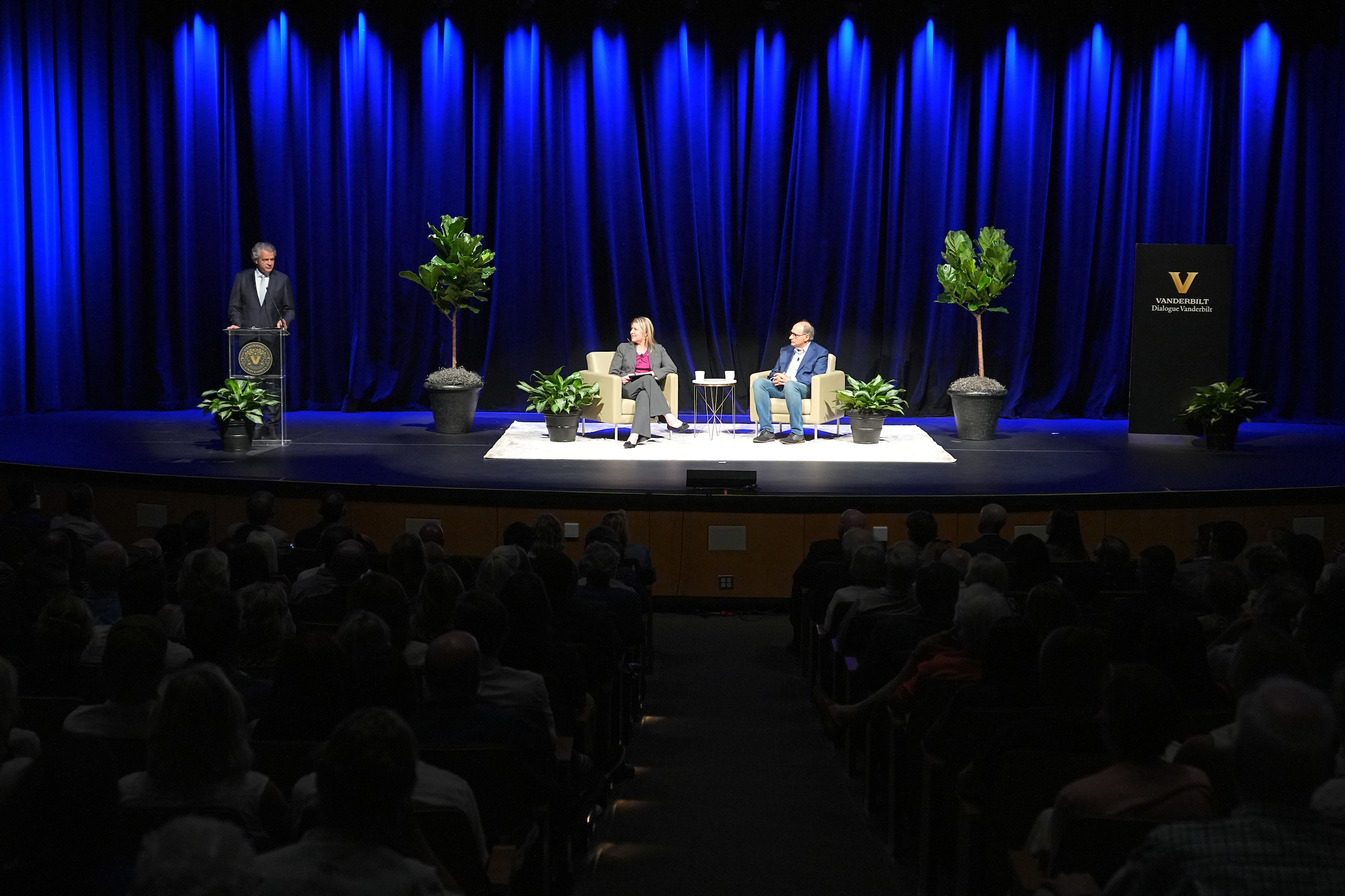 David Axelrod and Nicole Hemmer are seated in front of a blue curtain on stage. Chancellor Daniel Diermeier stands at a podium to the left. 