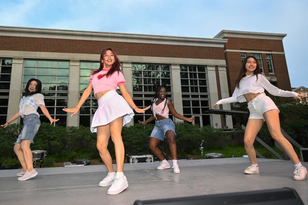 A group of girls dance on stage in front of a building.