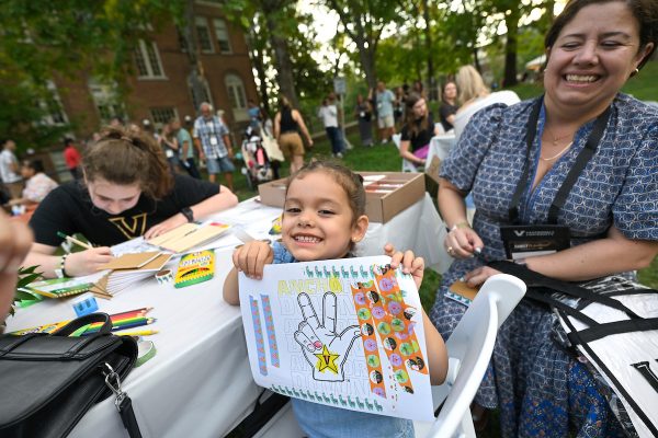 A child holds up a coloring sheet with the Vanderbilt hand symbol.