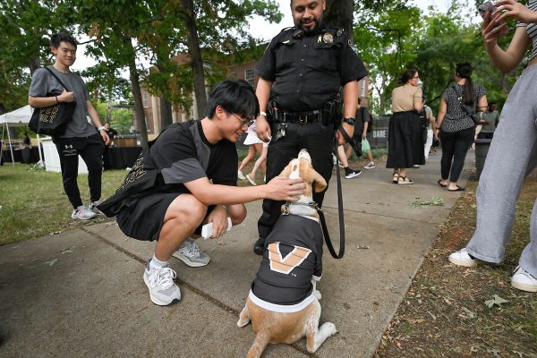 A student crouches to pet a dog wearing a Vanderbilt shirt.