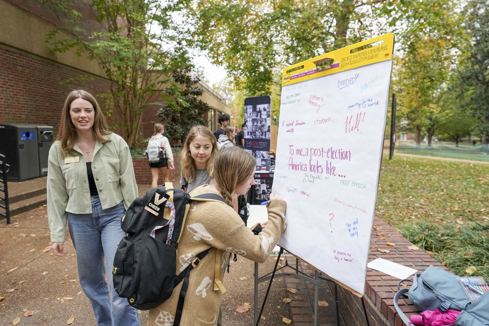 A female in a brown cardigan writes a message on a large pad of paper sitting on the Vanderbilt campus.