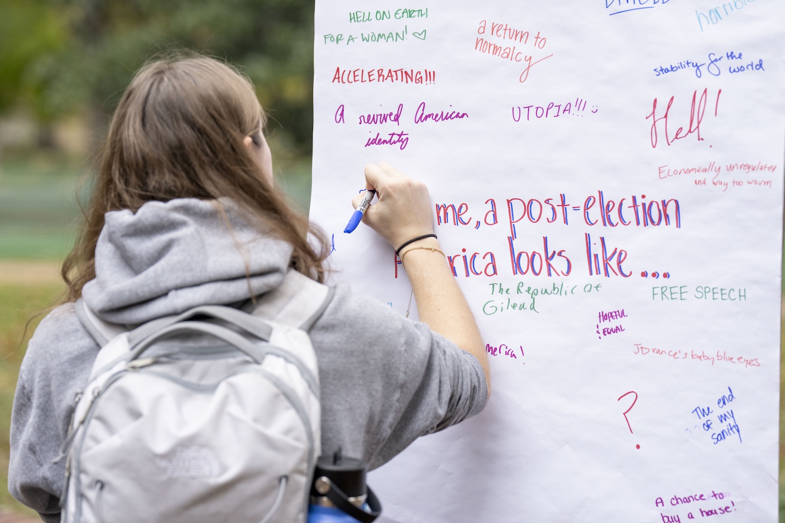 A female in a gray hoodie writes a message on a large white pad of paper. 