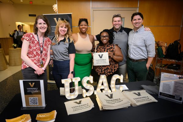 A group of men and women standing behind a booth with lit signage reading "USAC"