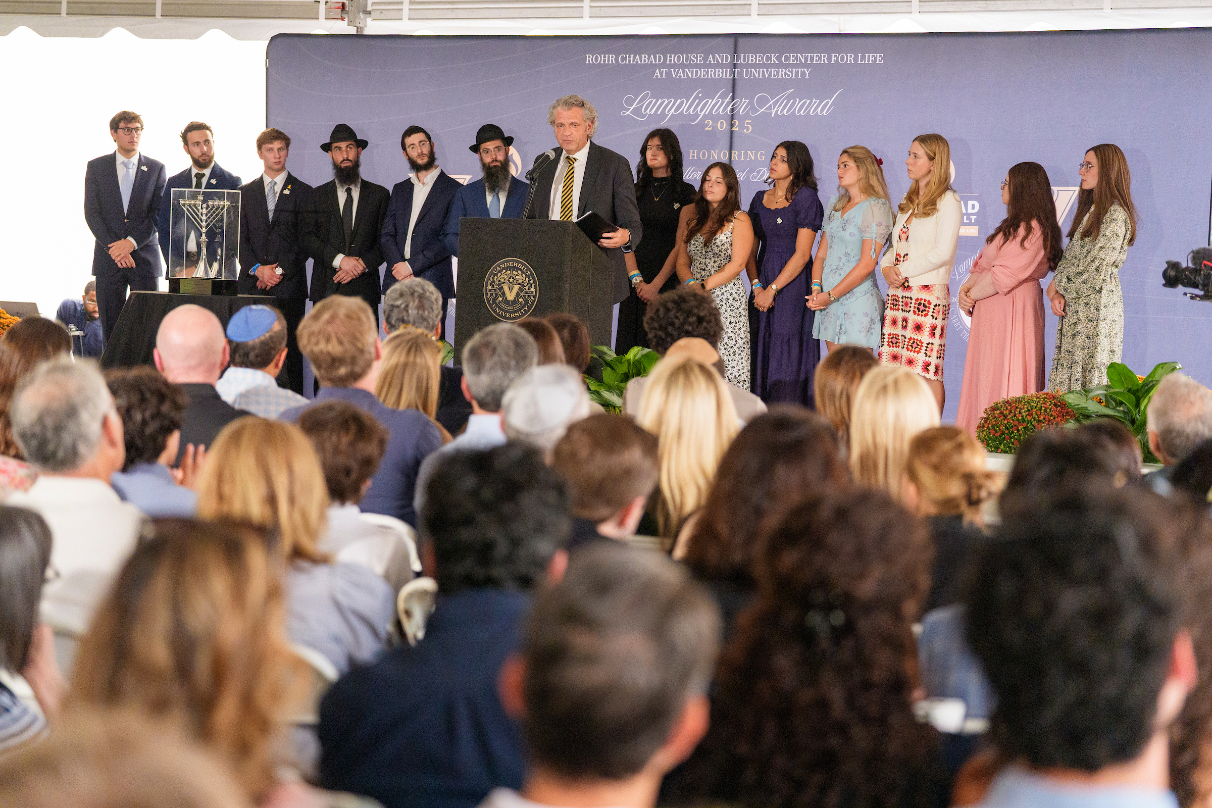 A man standing on a podium on stage surrounded by students.