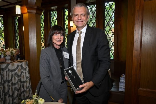 A man and a woman stand side by side with the man holding a white rose in a box