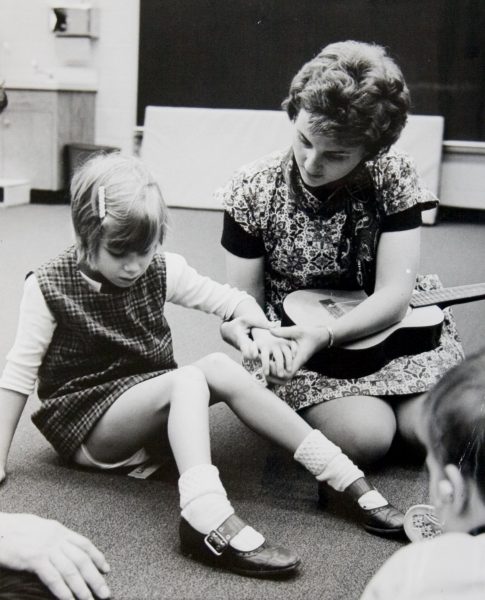A female teachers helps a young girl in a classroom.