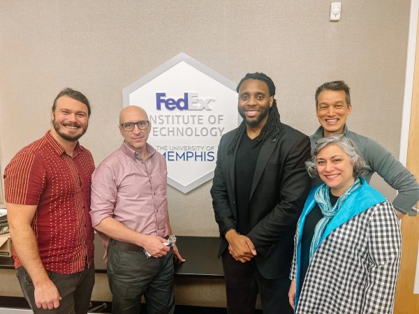 Charleson Bell stands with four colleagues from the University of Memphis by a sign for their FedEx Institute of Technology