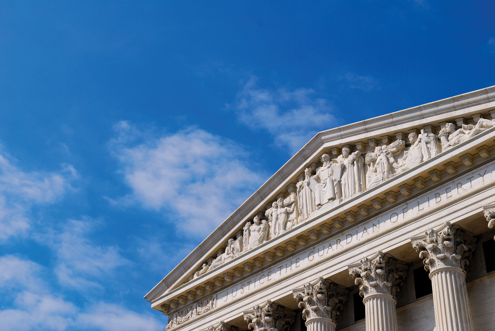 A view of the top of the building that houses the U.S. Supreme Court in Washington, DC, with blue sky behind.