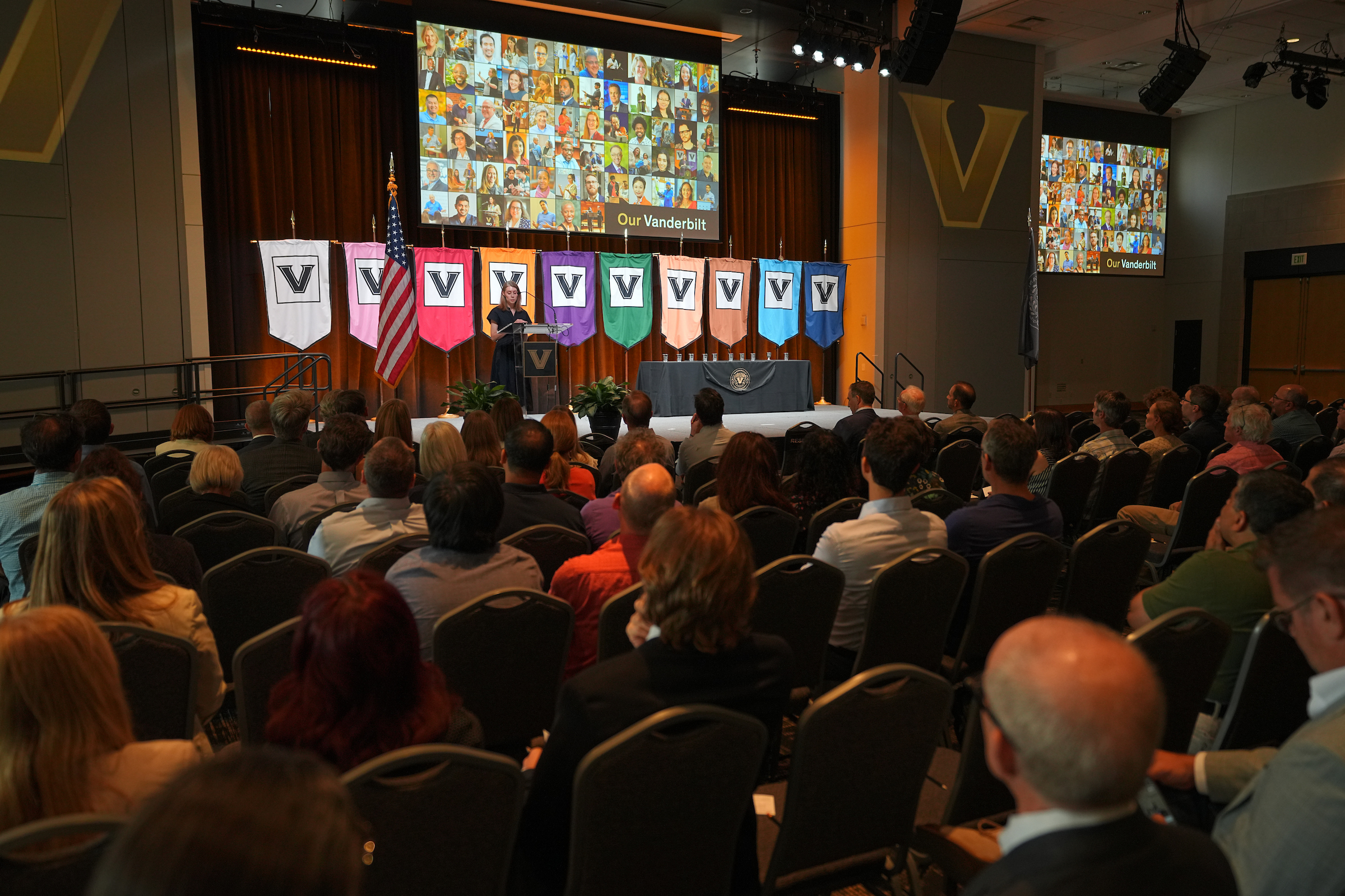 A seated audience in a conference room watching a slideshow presentation on stage.