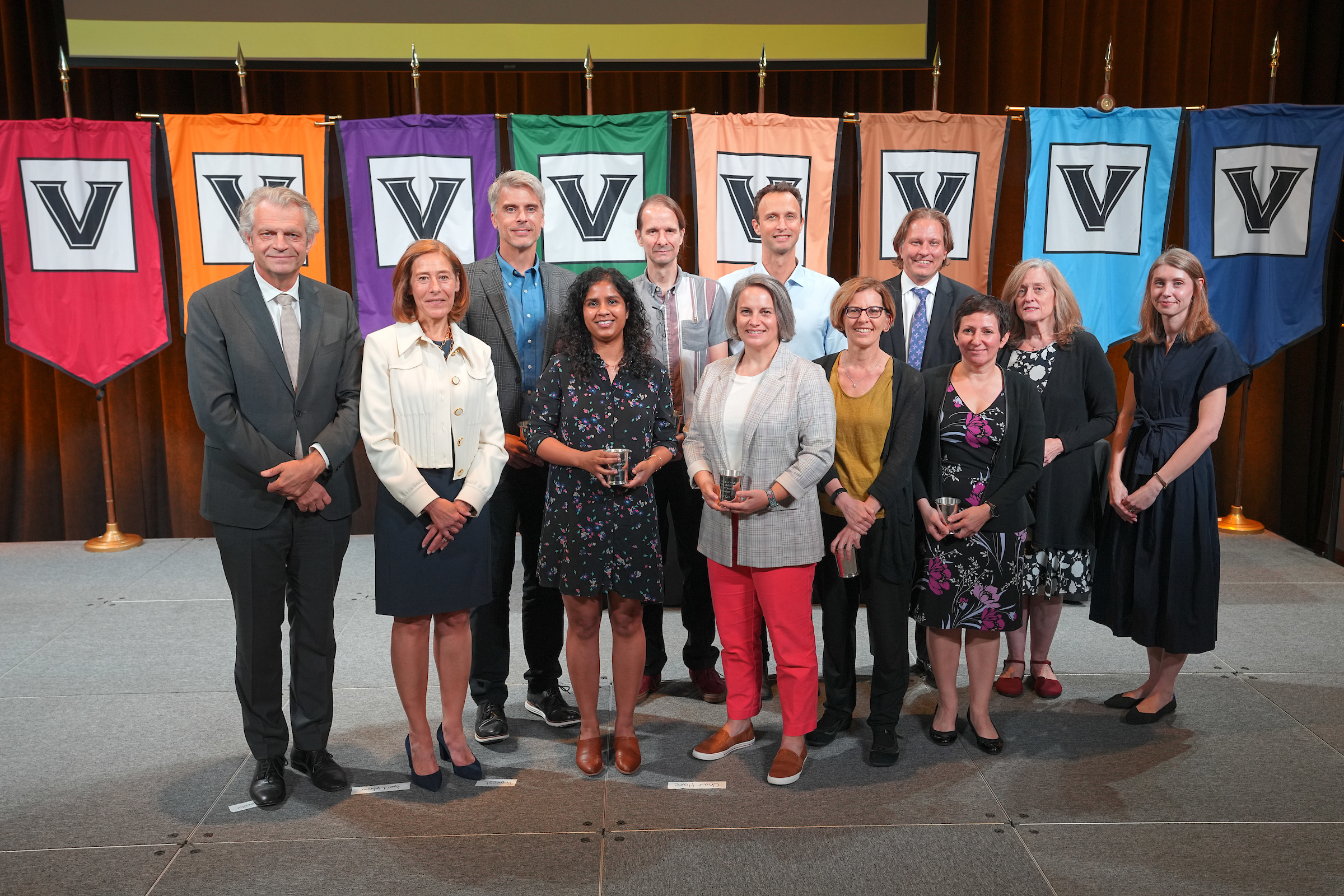 A group of men and women standing on a stage in front of multicolored Vanderbilt banners. 