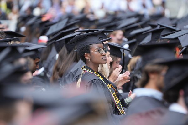 Graduates in black gowns and colorful stoles and cords listen to the Commencement proceedings at GEODIS park.