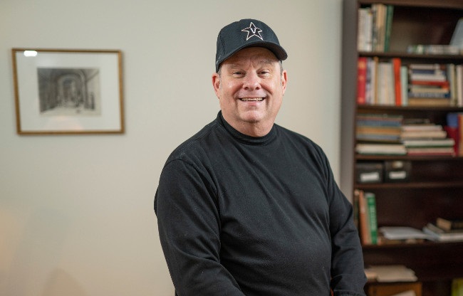 photograph of Christopher Johns wearing Vanderbilt baseball cap in his office at Cohen Hall
