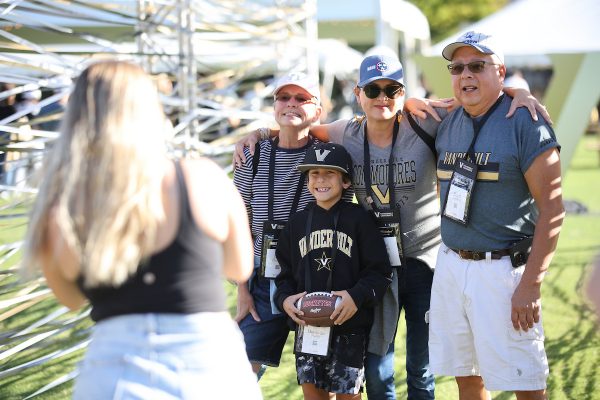 Two men, a woman, and a child wearing Vanderbilt gear smile for a woman taking a photo.