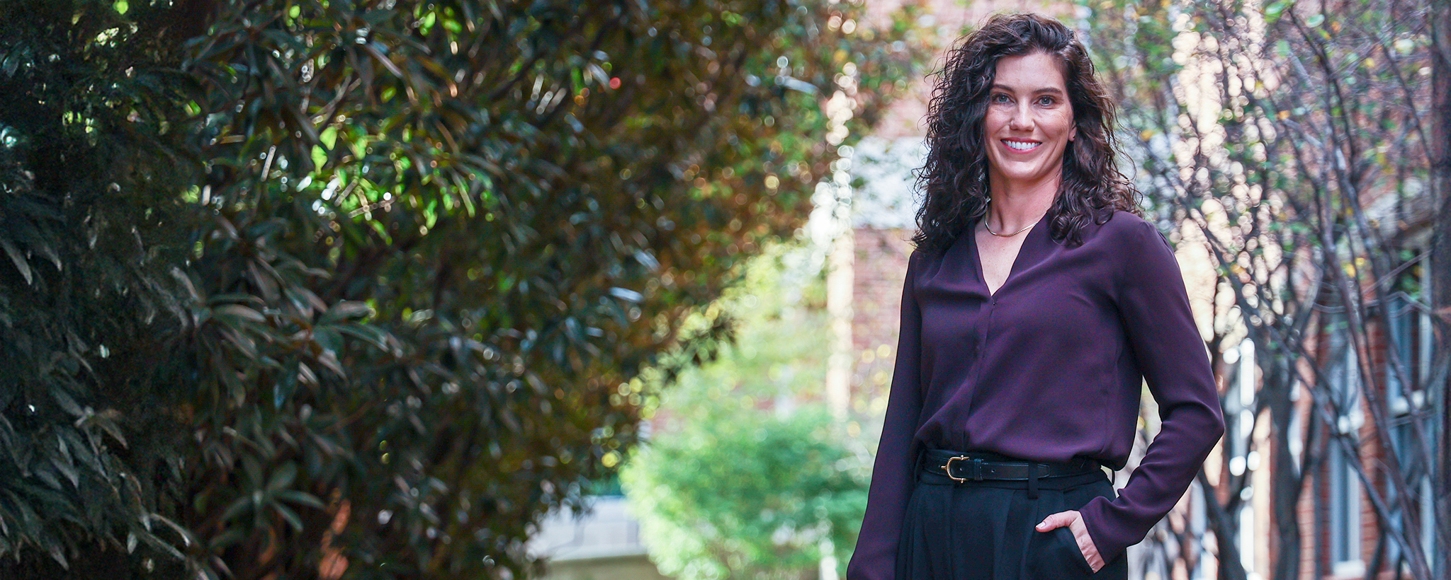 woman with wavy brown hair in purple blouse and black pants