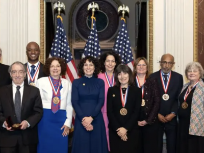 National Science Medal winners standing in a group together in front of three U.S. flags and a marble column