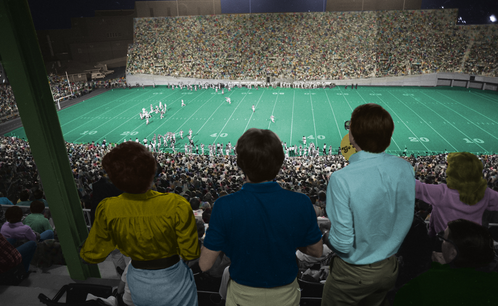 A colorized version of the black and white photo taken from high in the stands during the 1981 opening football game against Maryland with four fans in the foreground and players on the field in the distance. The stadium is packed.