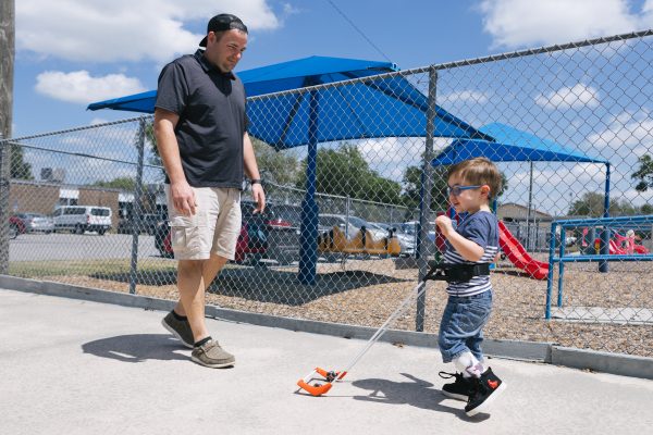 Adult male walks with a young boy who is using the belt cane.