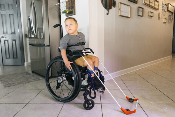 A young boy in a wheelchair uses the belt cane.