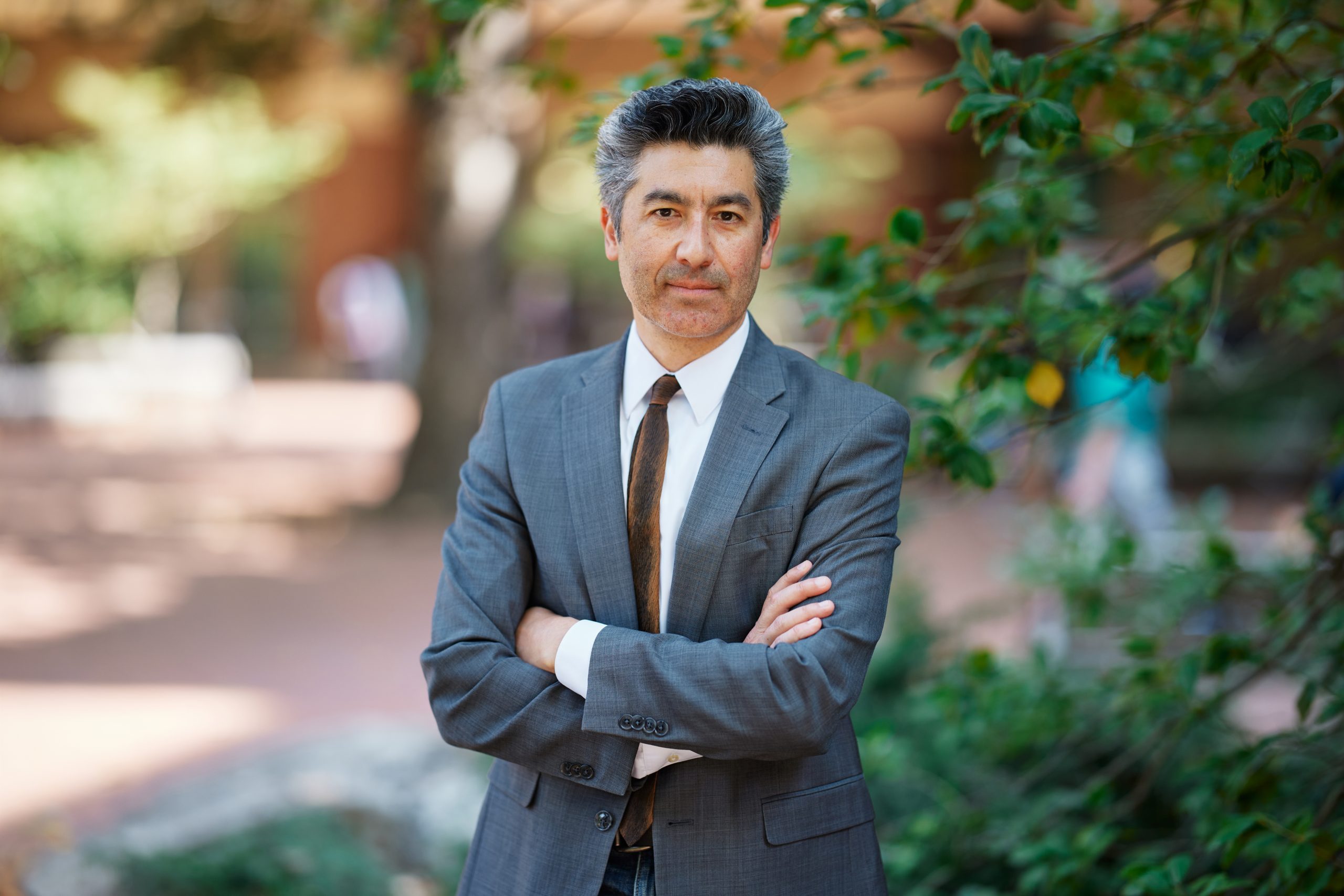 a man stands with his arms crossed in front of a building and trees