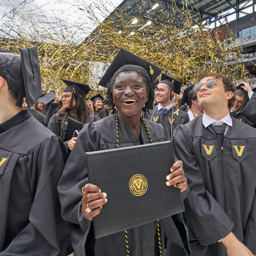 A student holding their Vanderbilt diploma as gold confetti falls in the distance.