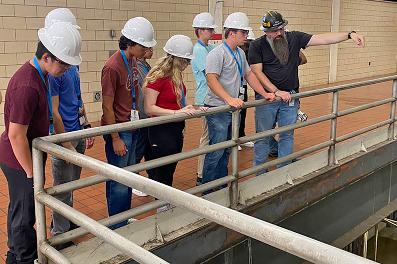 students and technicians standing in hard hats and talking