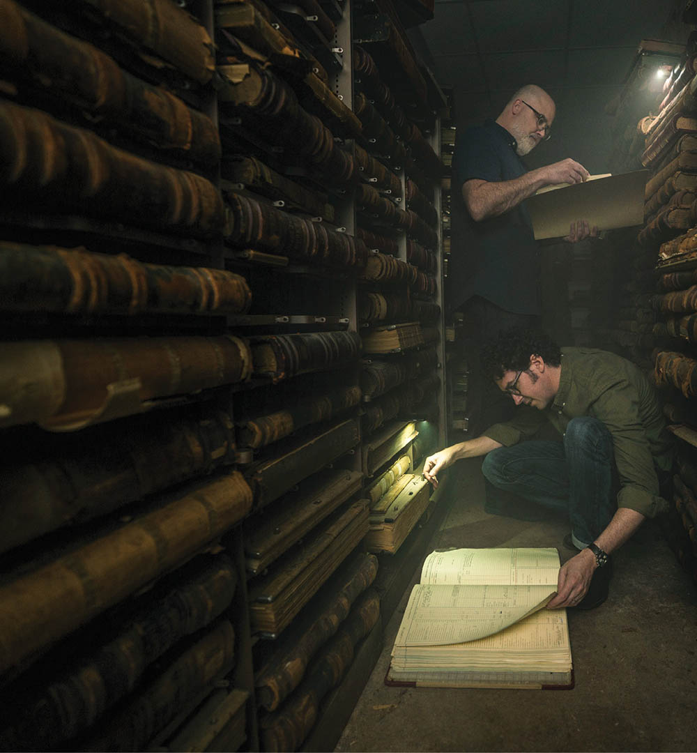 photo of Chip Brantley and Andrew Beck Grace reading old documents by flashlight in a dark room 