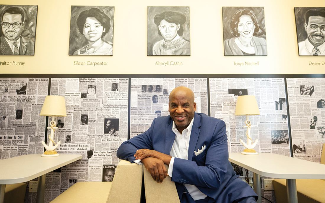 Artist James Threalkill sitting at a table with his paintings on the wall above him.