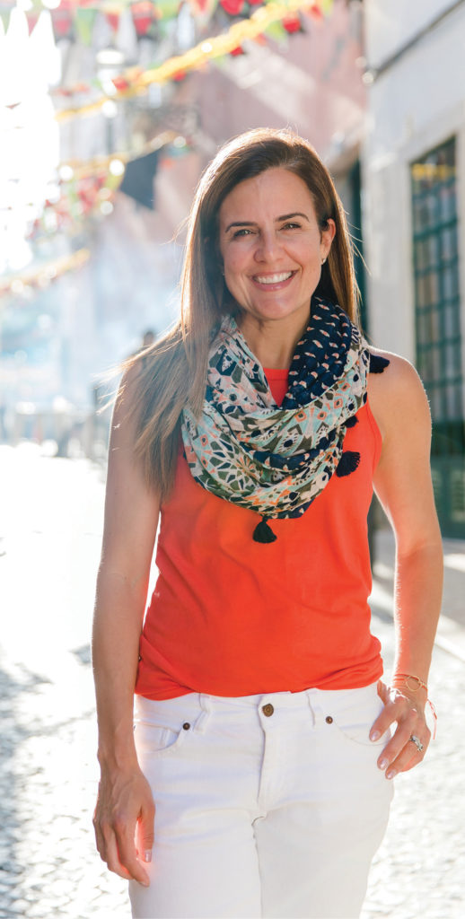 Nicole Feliciano, wearing orange blouse and white pants on a colorful street